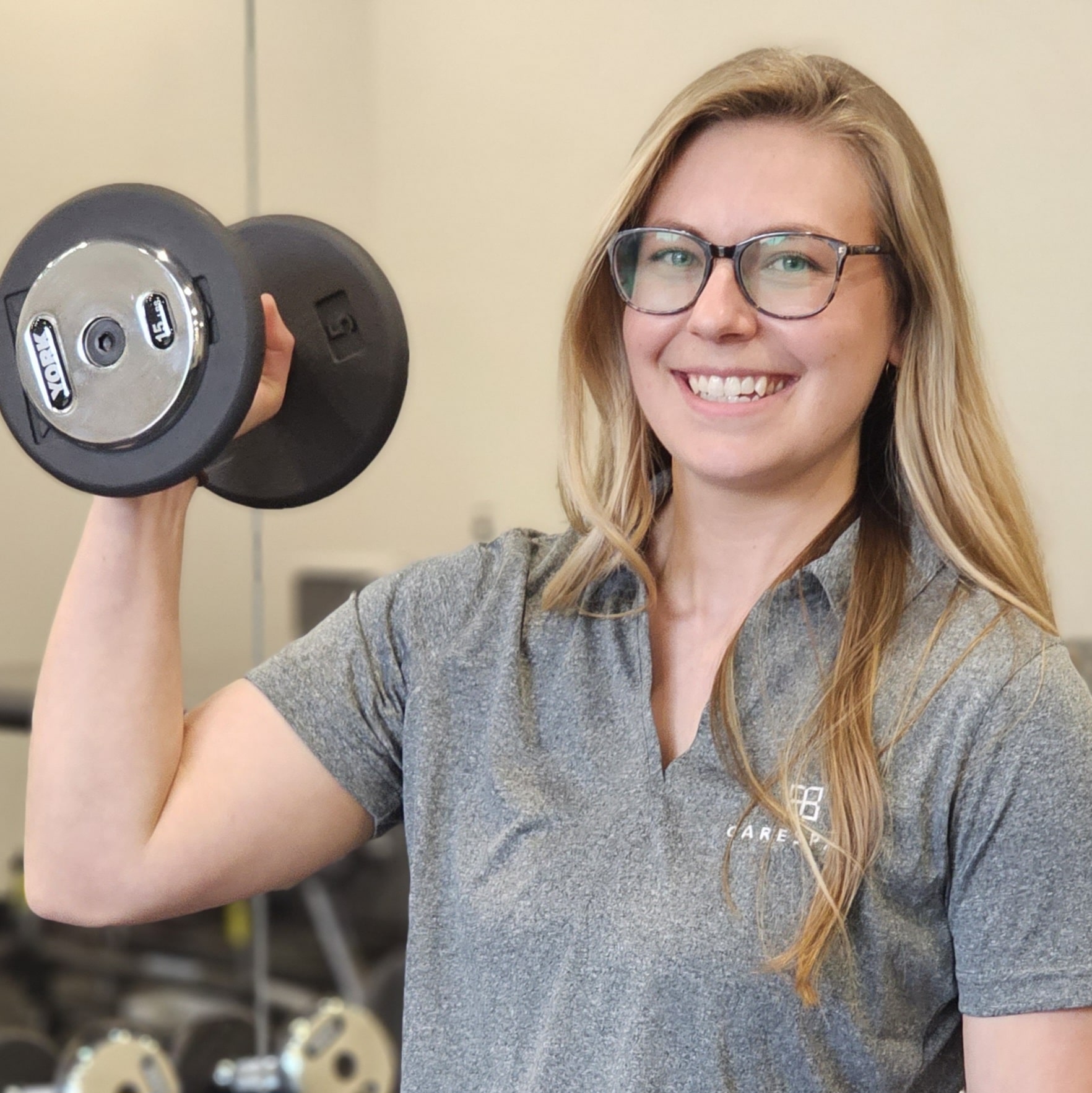 a female kinesiologist in Kitchener Waterloo working as a physiotherapist assistant and holding a dumbbell in the clinic gym